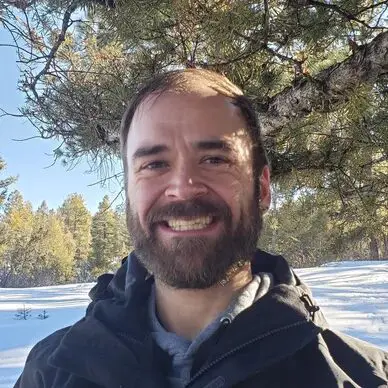 A man standing in the snow near a tree.